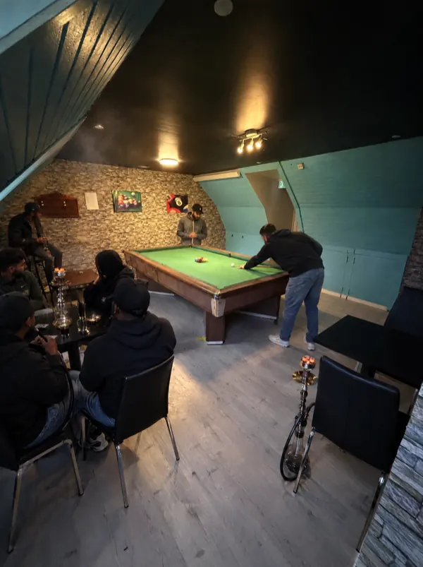 Ovenpå: en gruppe ved bordet med vandpibe, mens der spilles billard bagved